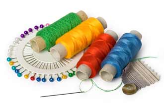 Photo of spools of colorful thread, a circle of pins, needle with green thread, and a brown button with brown striped fabric.